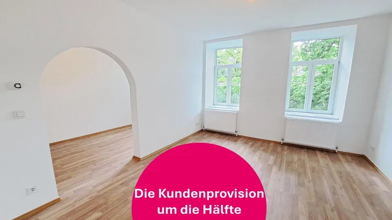 Heller, leerer Raum mit Laminatboden, zwei Fenstern und einem Rundbogen, der zu einem weiteren Bereich führt.