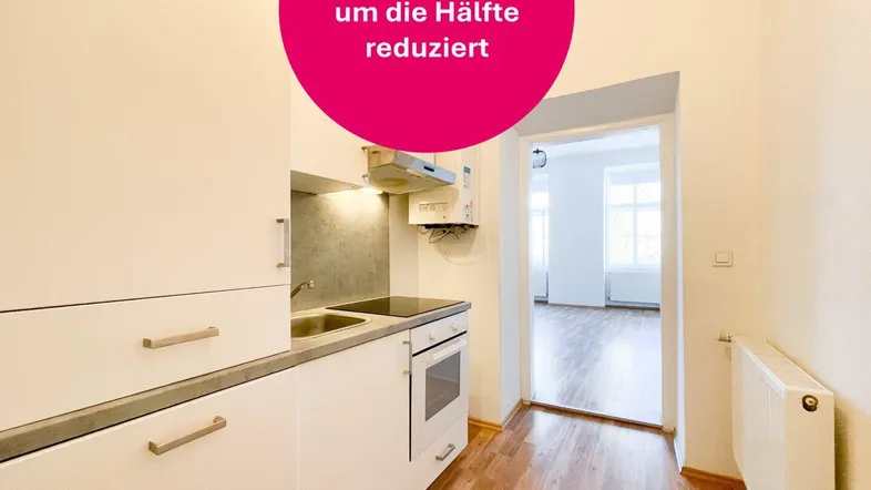 Kleine Einbauküche mit weißen Schränken und Blick in einen hellen Wohnraum mit Laminatboden.