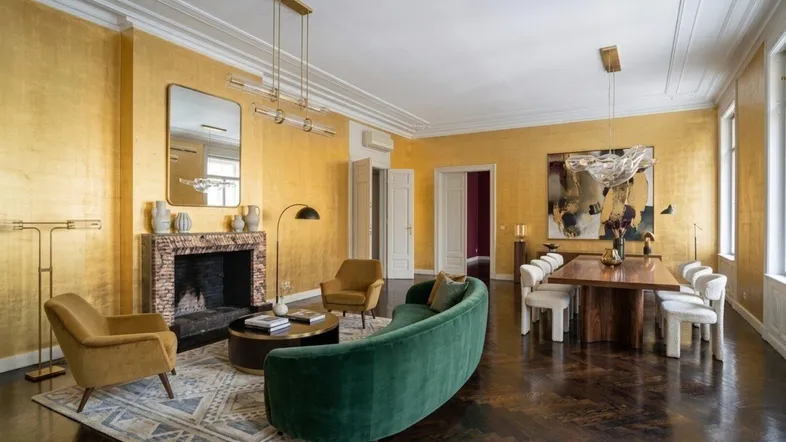 Luxuriöser Wohn- und Essbereich mit goldenen Wänden, Kamin und dunklem Fischgrätparkett.