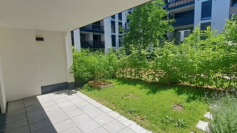 Geräumige Terrasse mit Fliesenboden und angrenzender Grünfläche, umgeben von Sträuchern.