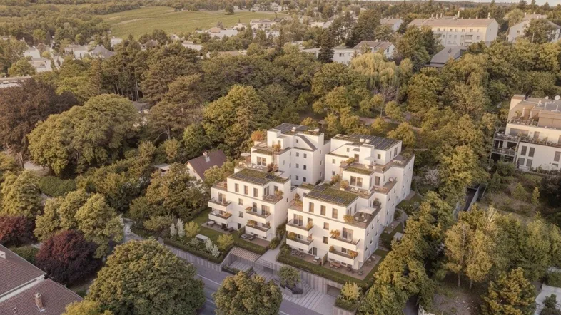 Luftaufnahme eines modernen Wohnkomplexes mit weißen Fassaden, Balkonen und grünen Dächern, umgeben von üppiger Natur.