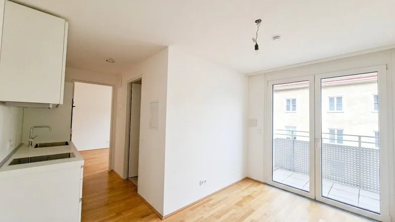Heller Wohnbereich mit Parkettboden und Zugang zu einem kleinen Balkon, ideal für ein modernes Apartment.