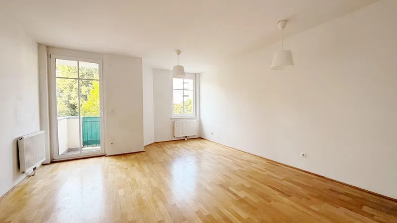 Geräumiges, helles Wohnzimmer mit Parkettboden und Zugang zu einem Balkon.