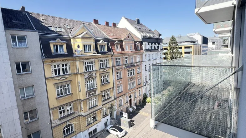 Weitblick von einem Balkon auf eine Stadtstraße mit Gebäuden und parkenden Autos.