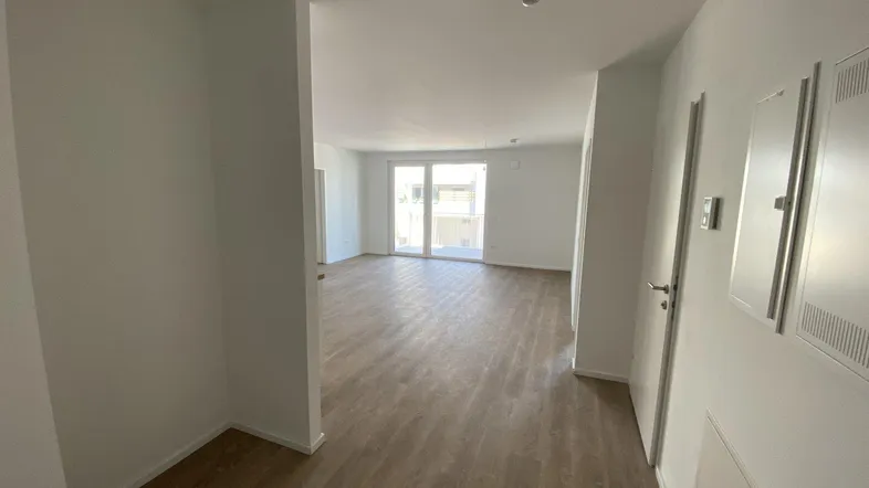 Heller Flur mit Laminatboden, der zu einem lichtdurchfluteten Wohnbereich mit Balkonzugang führt.