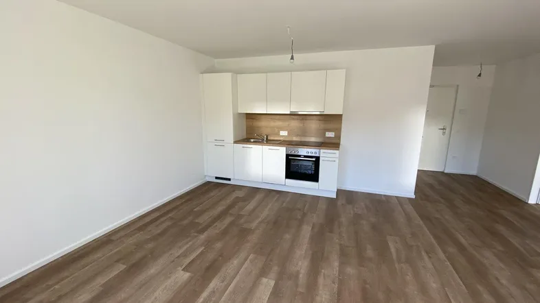 Heller Wohnraum mit integrierter Küchenzeile und modernem Laminatboden in einem Neubau.