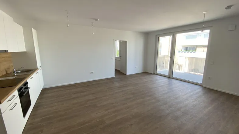 Helles, offenes Wohnzimmer mit integrierter Küche, modernem Boden und Zugang zum Balkon.