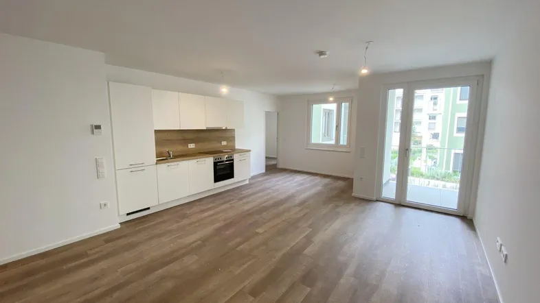 Heller, offener Wohnbereich mit integrierter Küche, Laminatboden und Zugang zum Balkon.