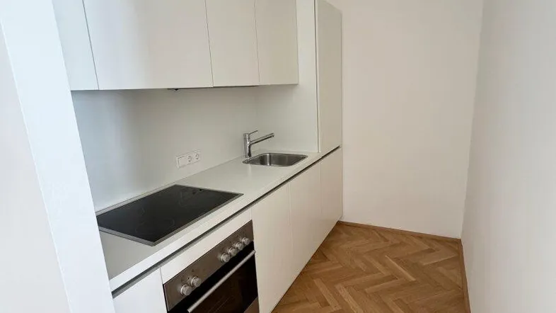 Moderne, kompakte Küchenzeile mit weißen Schränken, Kochfeld und Backofen in einem hellen Raum.