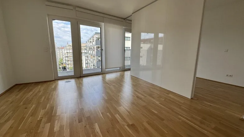 Helles Wohnzimmer mit Parkettboden und Zugang zu einem Balkon, bietet viel natürliches Licht.