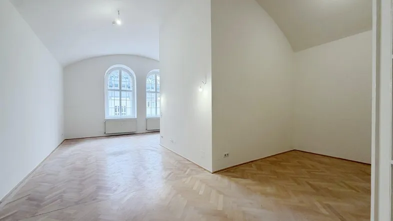 Helles Zimmer mit Fischgrätparkett, hohen Decken und eleganten Rundbogenfenstern, bereit zur Einrichtung.