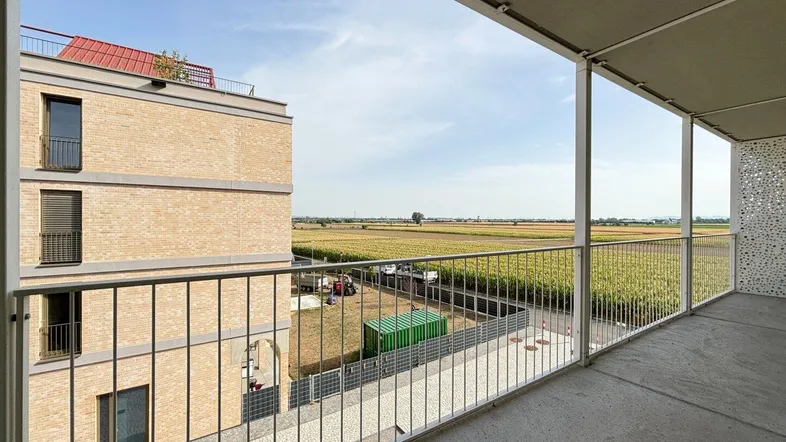 Geräumiger Balkon mit weitem Blick über Felder und angrenzende moderne Gebäude.