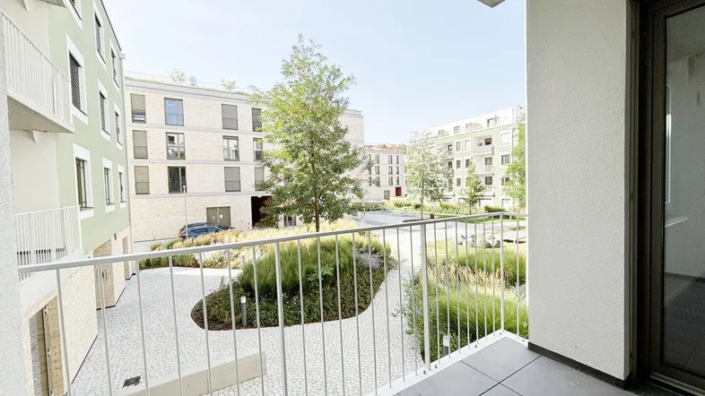 Balkon mit Blick auf den begrünten Innenhof und die umliegenden Neubauten.