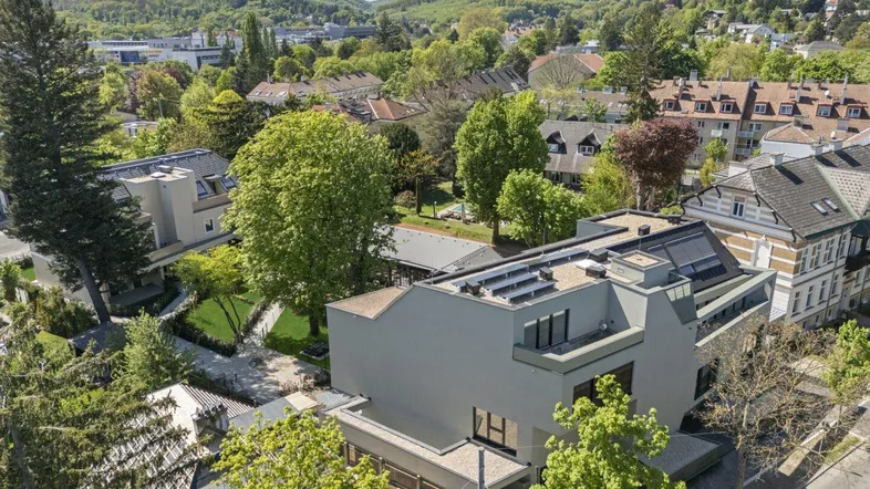 Moderne Stadtvilla mit Flachdach, Photovoltaikanlage und großzügigen Balkonen, umgeben von viel Grün.