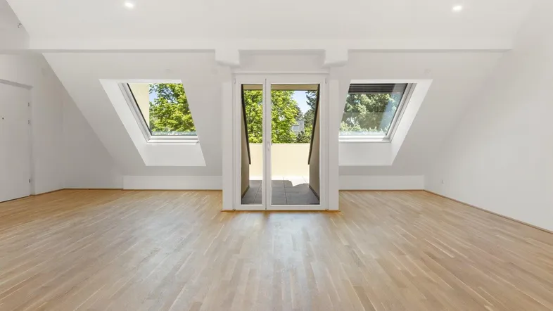 Heller Dachgeschossraum mit Holzboden, Dachfenstern und Zugang zu einem kleinen Balkon.