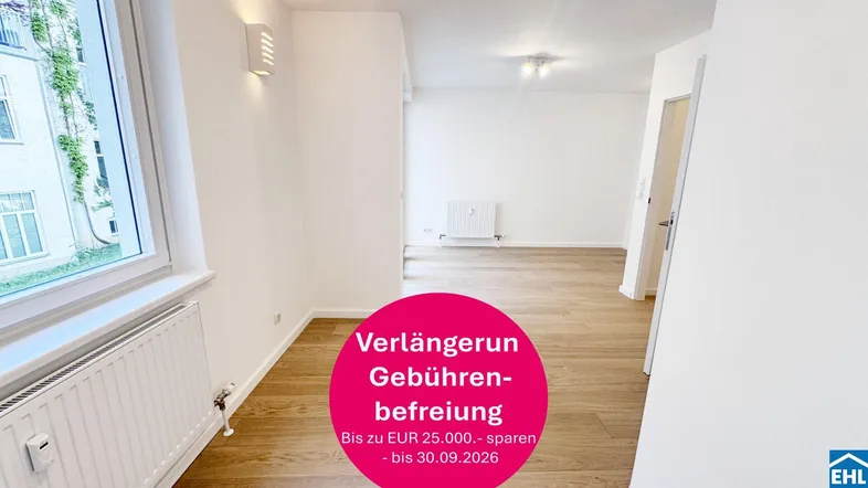 Heller, leerer Raum mit Holzfußboden, weißen Wänden und Fensterblick ins Grüne.