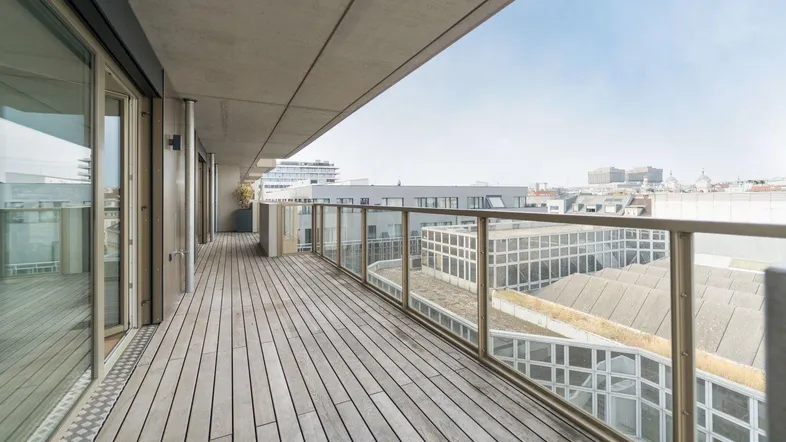 Großer Balkon mit Holzboden, Glasgeländer und weitem Blick über die Stadt.
