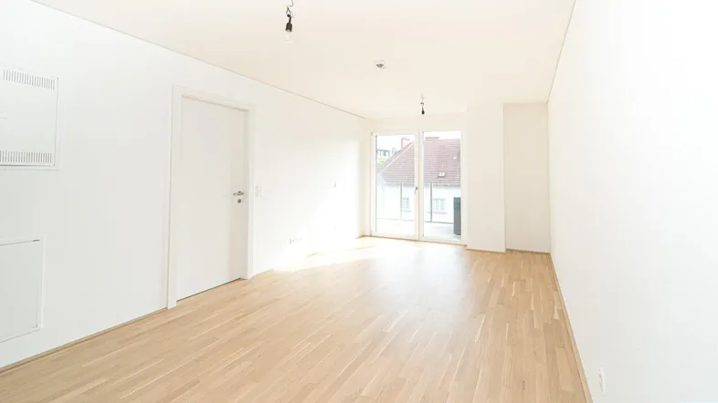 Helles, leeres Zimmer mit Holzboden und Zugang zu einem Balkon, ideal für Wohn- oder Schlafbereich.
