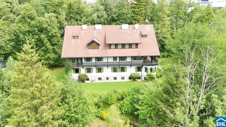 Großes Anwesen umgeben von üppiger grüner Natur und hohen Bäumen mit traditionellem Dach.