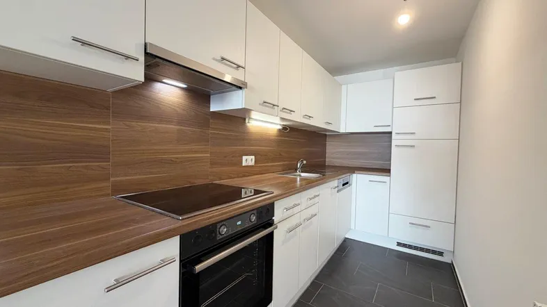 Moderne Küche mit weißen Schränken, Holzoptik-Arbeitsplatte und dunklen Fliesenboden.