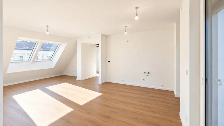 Helles, leeres Zimmer mit Holzboden, weißen Wänden und Dachfenstern, ideal als Wohnbereich.