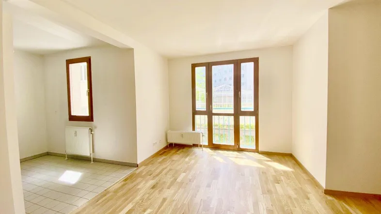 Helles Wohnzimmer mit Parkettboden, weißen Wänden und Zugang zu einem gefliesten Bereich.
