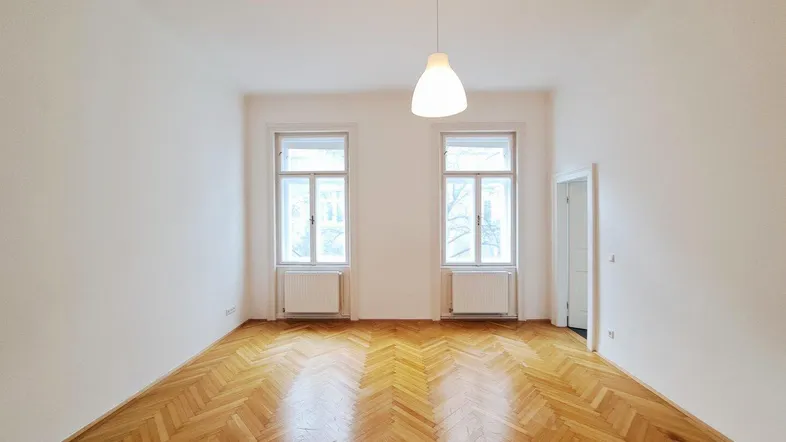 Heller, frisch renovierter Raum mit klassischem Fischgrätparkett und hohen Fenstern, ideal als Wohnzimmer.