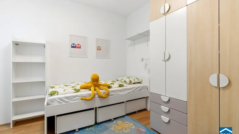 Helles Kinderzimmer mit Einzelbett, Stauraum und einem bunten Teppich.