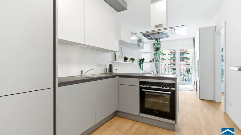 Moderne Küche mit hellgrauen Fronten, Holzboden und integriertem Backofen, offen zum Wohnbereich.