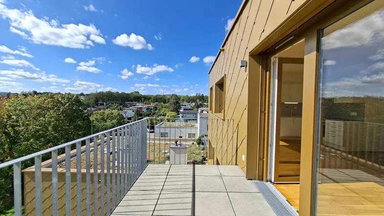 Geräumige Terrasse mit Fliesenboden und weitem Blick über die Umgebung und grüne Bäume.