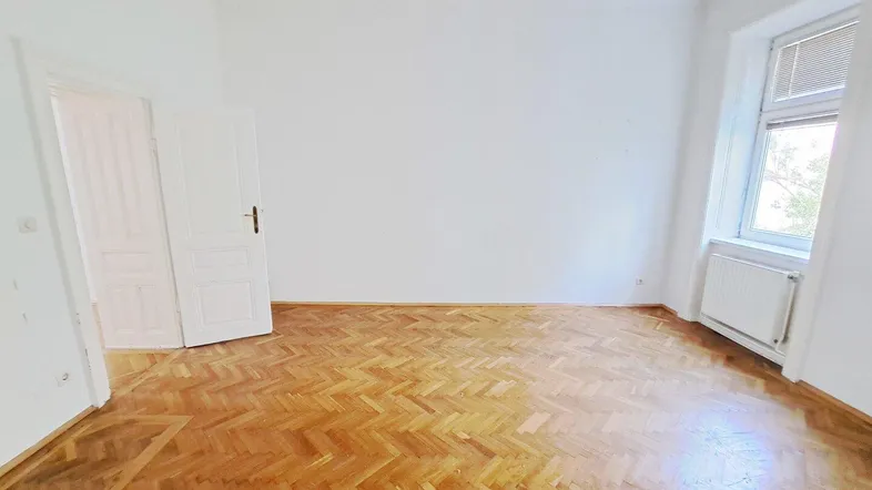Helles, leeres Zimmer mit klassischem Fischgrätparkett und einem Fenster.