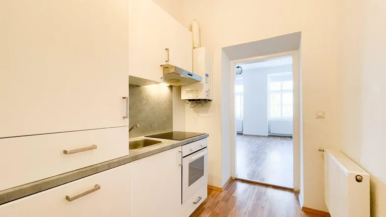 Funktionale Einbauküche mit weißen Schränken, integriertem Backofen und Blick in einen hellen Wohnraum.