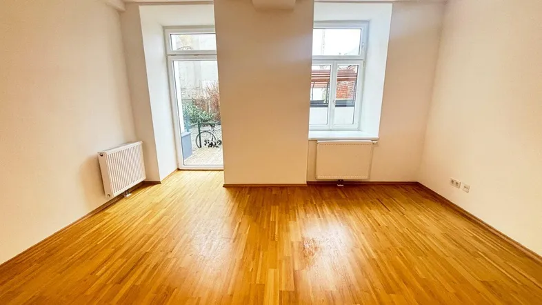 Heller Raum mit Parkettboden, großen Fenstern und Zugang zu einem Außenbereich.