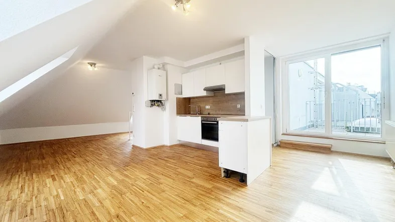 Heller offener Wohnbereich mit integrierter weißer Küche, Holzboden und Zugang zu einem Balkon.