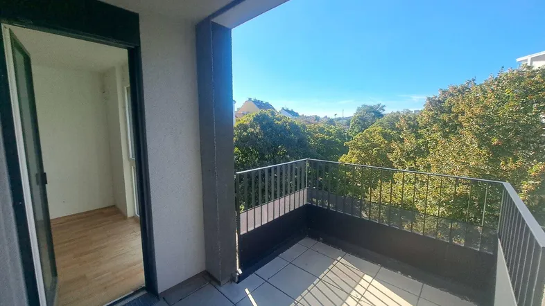 Sonniger Balkon mit Fliesenboden und weitem Blick ins Grüne.
