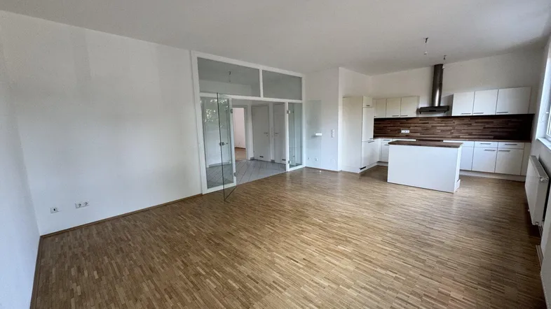 Heller offener Wohnbereich mit integrierter Küche, Parkettboden und viel Tageslicht.