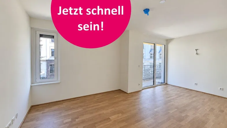 Heller, leerer Wohnraum mit Parkettboden, großen Fenstern und Zugang zum Balkon.