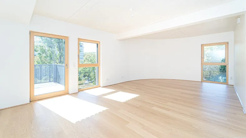 Helles Wohnzimmer mit Holzboden, großen Fenstern und Zugang zu einem Balkon.
