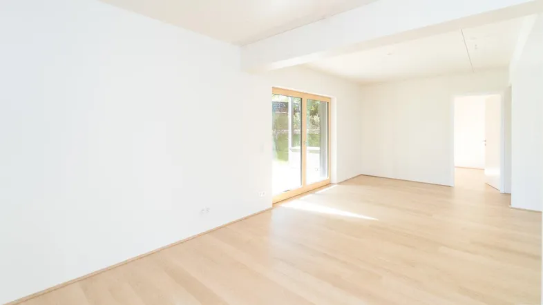 Helles, leeres Zimmer mit Holzboden und Zugang zu einer Terrasse oder Garten.