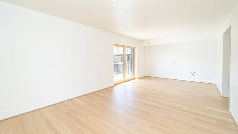 Helles, leeres Wohnzimmer mit Parkettboden und Zugang zu einem Balkon, bereit zur individuellen Gestaltung.