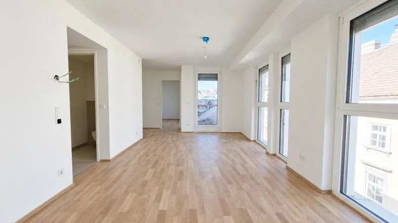 Geräumiges, helles Wohnzimmer mit Laminatboden und Zugang zu einem weiteren Raum, ideal für neue Bewohner.