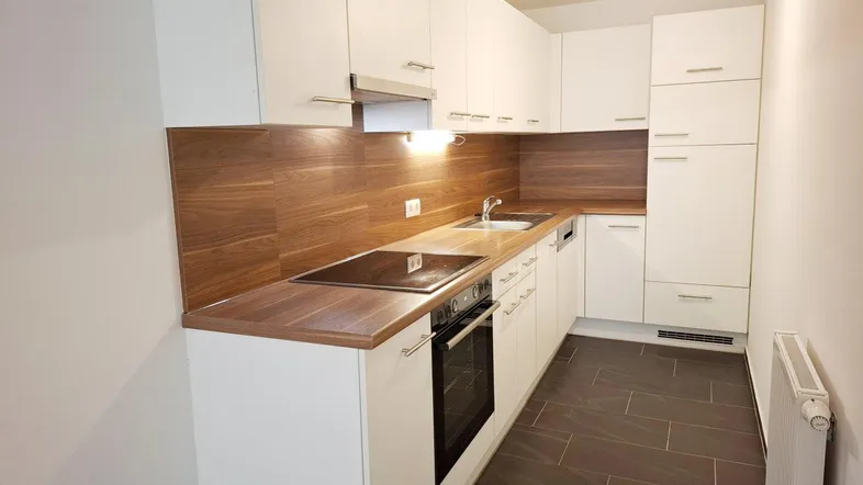Moderne Einbauküche mit weißen Hochglanzfronten, Holzoptik-Arbeitsplatte und dunklem Fliesenboden.