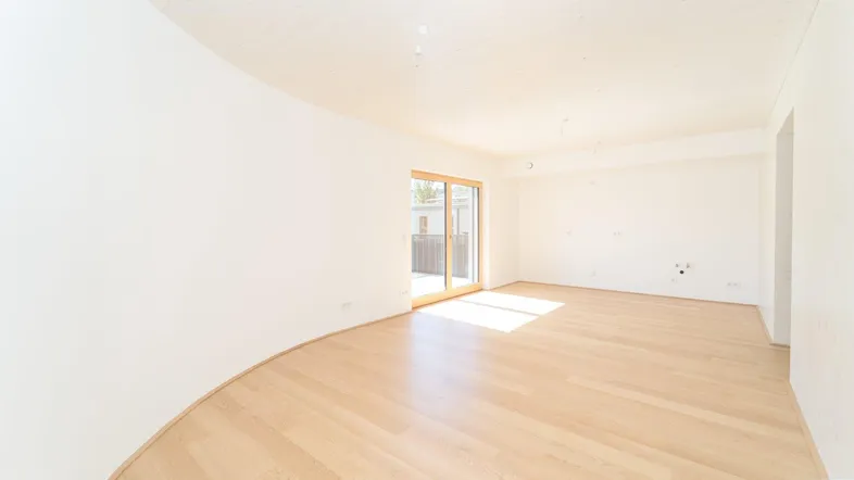 Lichtdurchfluteter Wohnbereich mit hellem Parkettboden und Zugang zu einem Balkon.