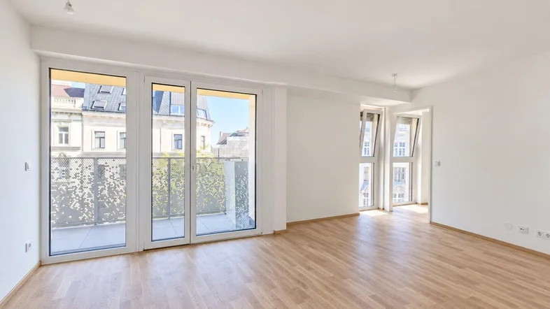 Helles, leeres Zimmer mit Parkettboden und Zugang zu einem Balkon, ideal für Wohn- oder Schlafbereich.