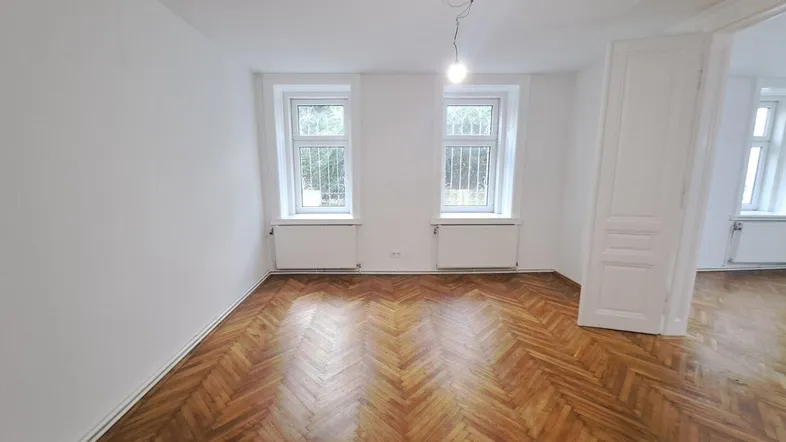 Helles Zimmer mit Fischgrätparkettboden und zwei Fenstern, bereit zur individuellen Gestaltung.