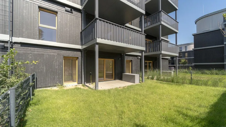 Erdgeschosswohnung mit privatem Gartenbereich und kleiner Terrasse vor der modernen Fassade des Gebäudes.