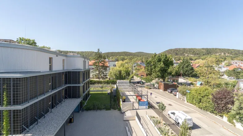 Blick von oben auf die moderne Wohnanlage mit Parkplätzen, Zufahrtsrampe und grüner Umgebung.