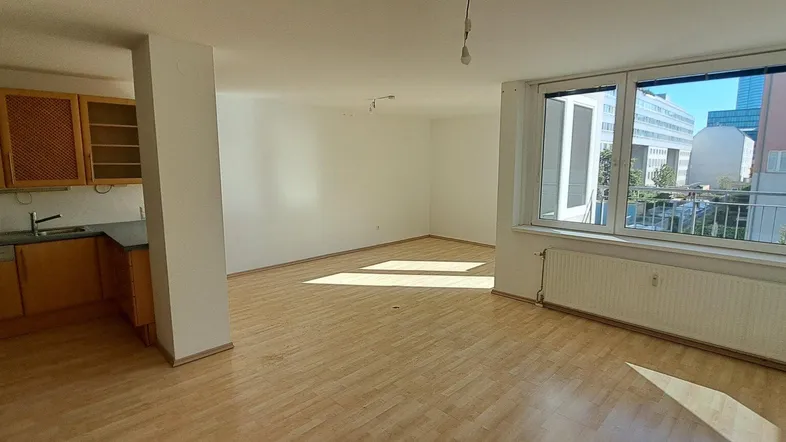 Heller Wohn- und Küchenbereich mit Holzfußboden und großen Fenstern, die viel Tageslicht hereinlassen.