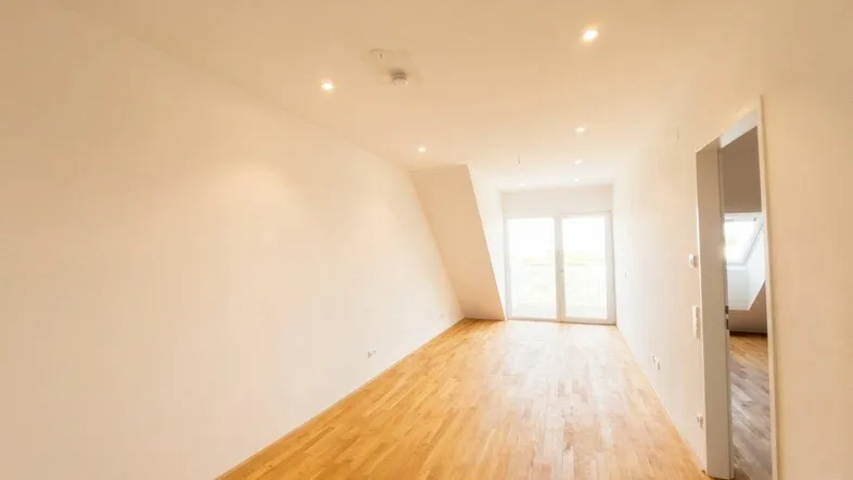 Helles Dachgeschosszimmer mit Holzboden und Zugang zu einem Balkon, ideal als Wohn- oder Schlafbereich.