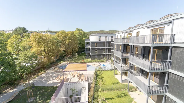Moderne Wohngebäude mit Balkonen, umgeben von Grünflächen und einem Gemeinschaftsspielplatz.